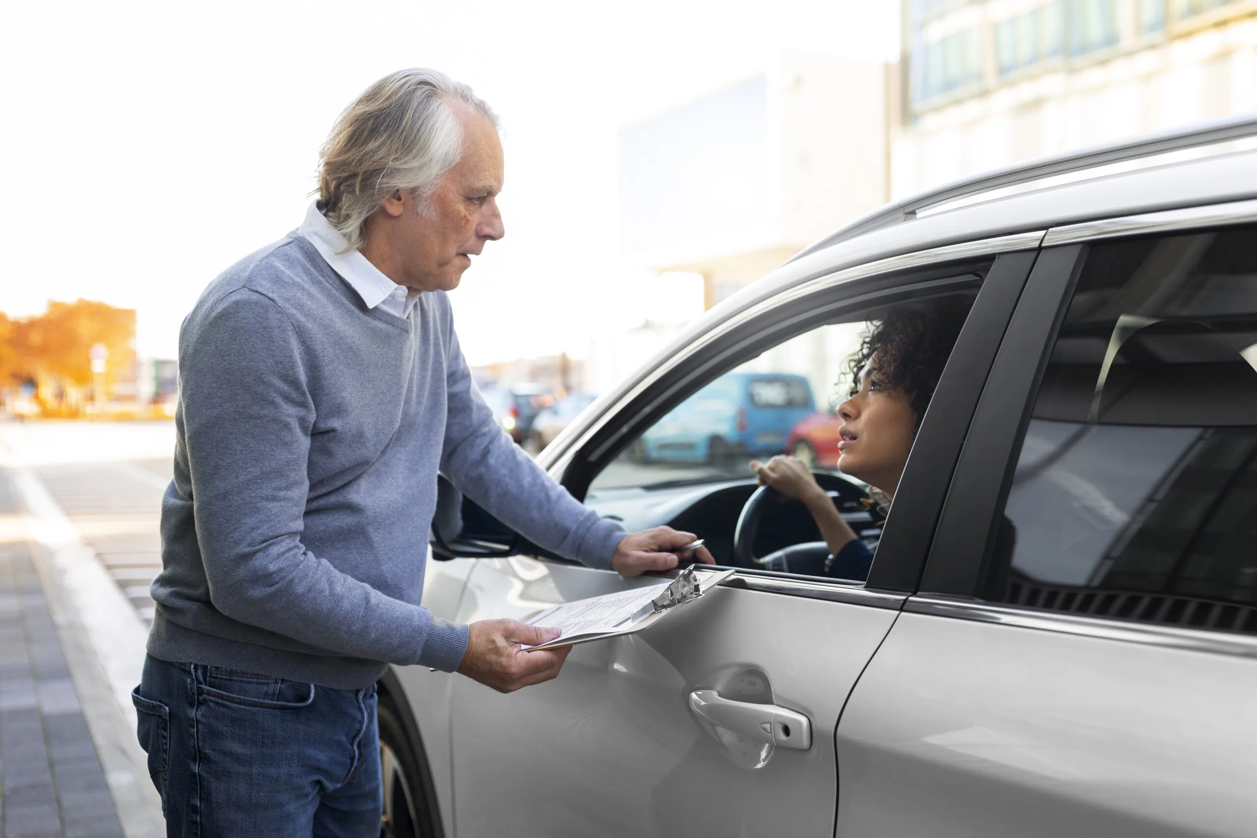 A driver speaking with someone holding a clipboard beside her car